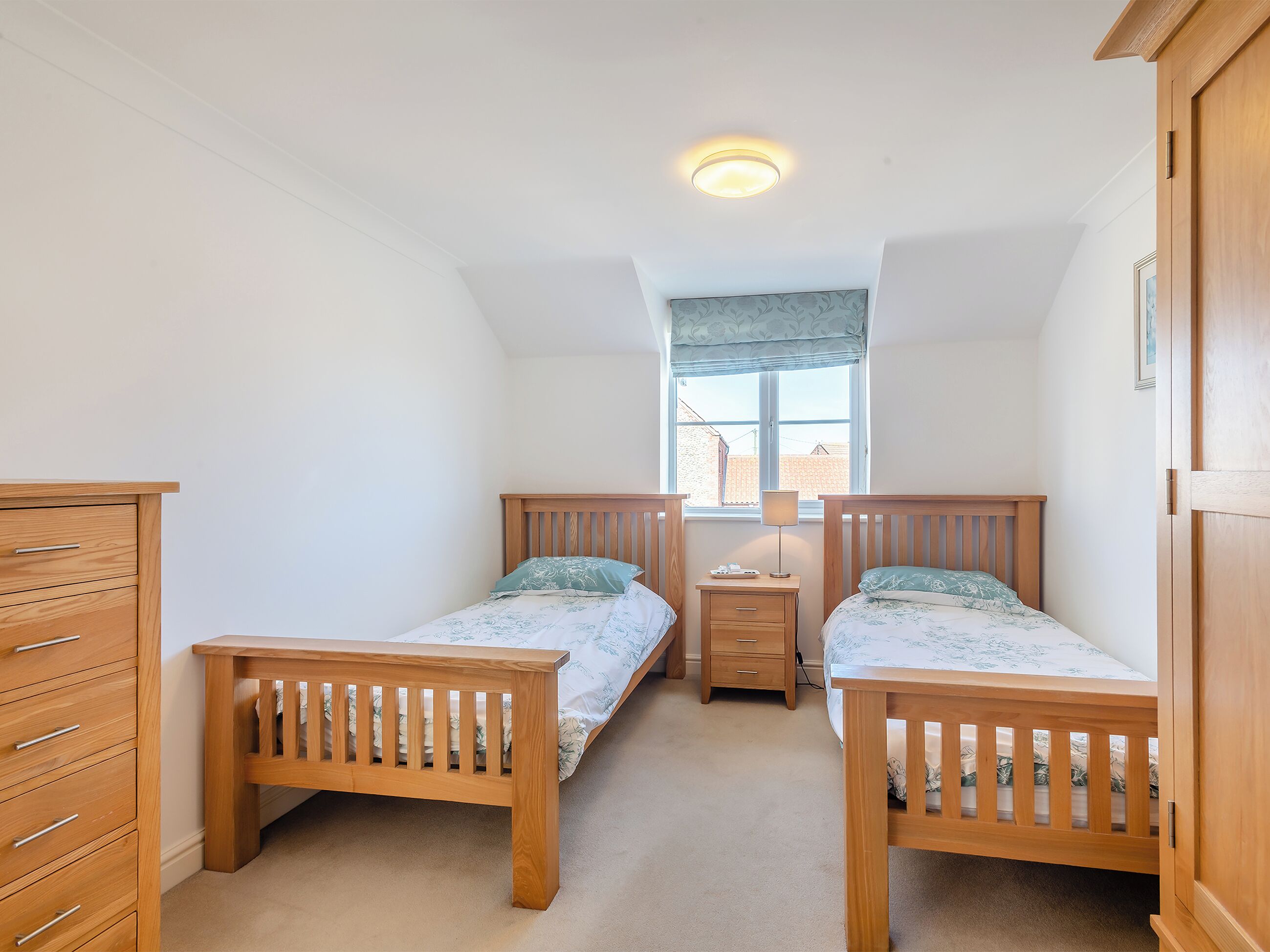 Ein kleines, gut beleuchtetes Schlafzimmer mit zwei Holzbett, einem Nachttisch und einer Holzkommode.