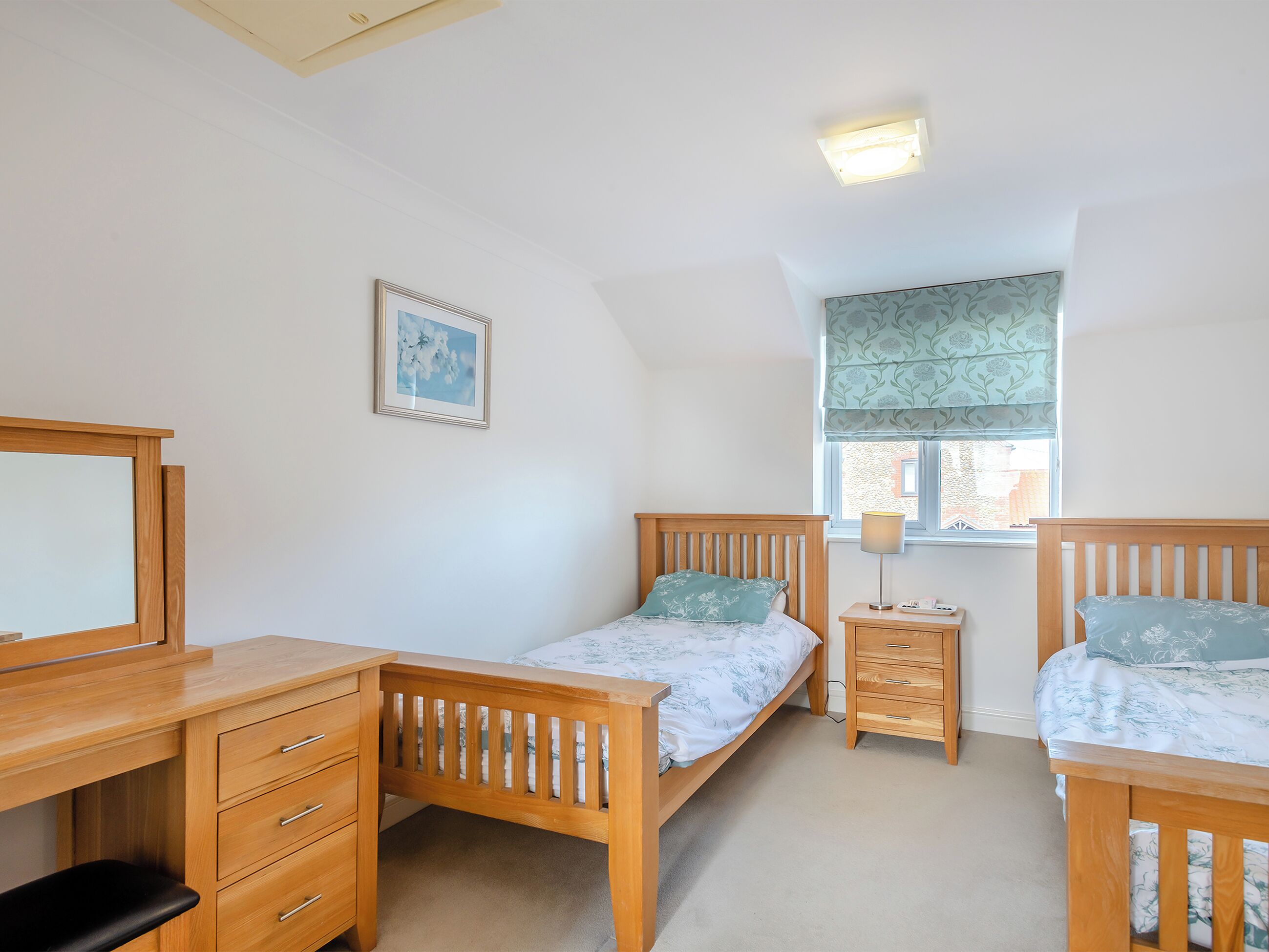 A bedroom with a wooden bed, a desk, and a dresser. There is a window with a view of buildings outside.