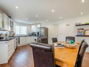 A modern kitchen with white cabinets, a built-in oven, microwave, and washing machine. There is a dining area with a wooden table and chairs. - 3 bedroom accommodation in Bacton (Bacton)