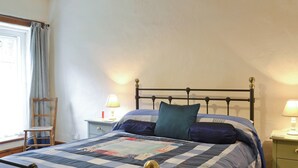 Un lit bien fait, recouvert d’une courtepointe, une chaise en bois, une table de chevet avec une lampe et une fenêtre avec des rideaux.
