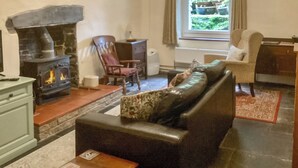 Un salon chaleureux avec une cheminée, un canapé, un fauteuil et une fenêtre donnant sur un paysage verdoyant.