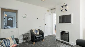 Een woonkamer met een open haard, een zwarte leren fauteuil, een ronde spiegel en een lamp met een stervorm.
