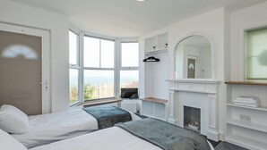 Een slaapkamer met twee bedden, een open haard, een groot raam en uitzicht op het omliggende landschap.