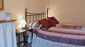 Et soveværelse med en seng, et natbord med en lampe og et lille bord med kande og tallerken.