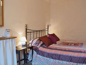 Ein Schlafzimmer mit einem Bett, einem Nachttisch mit Lampe und einem kleinen Tisch mit Krug und Teller.