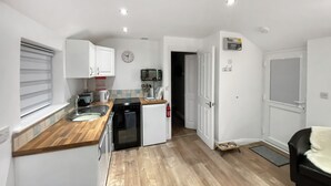 Eine kompakte Küche mit Spüle, Herd und Geschirrspüler, ein Essbereich mit Tisch und Stühlen sowie ein Wohnbereich mit einer Couch.