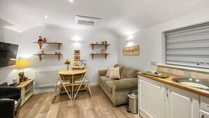 Ein kompakter Wohnbereich mit Esstisch, Sofa, Küchenzeile und dekorativen Regalen.