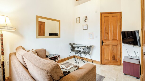 Een woonkamer met een bank, een eettafel met stoelen, een televisie en een houten deur.