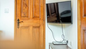 Een houten deur met een zwarte hendel, een flatscreen televisie aan de muur en een klein tafeltje met een laptop en stroomkabel.