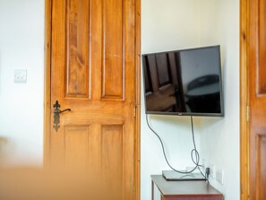 A wooden door with a black handle, a flat-screen TV mounted on the wall, and a small table with a laptop and power cord. - Thompsons Arms Cottages No2 (Flaxton, near York)