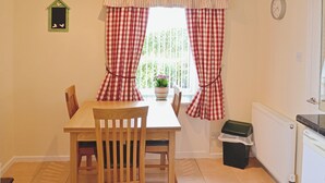 A dining area with a table and chairs, a window with checkered curtains, a clock on the wall, and a radiator. - 3 bedroom accommodation in Haddington (Haddington)