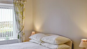 A neatly made bed with white bedding, a bedside table with a lamp, and a window with a curtain. - 3 bedroom accommodation in Haddington (Haddington)