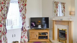A living room with a flat-screen TV on a wooden stand, a fireplace, and a purple rug. - 3 bedroom accommodation in Haddington (Haddington)