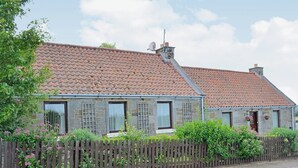A two-story stone house with a tiled roof, wooden fence, and a garden with pink flowers. - 3 bedroom accommodation in Haddington (Haddington)