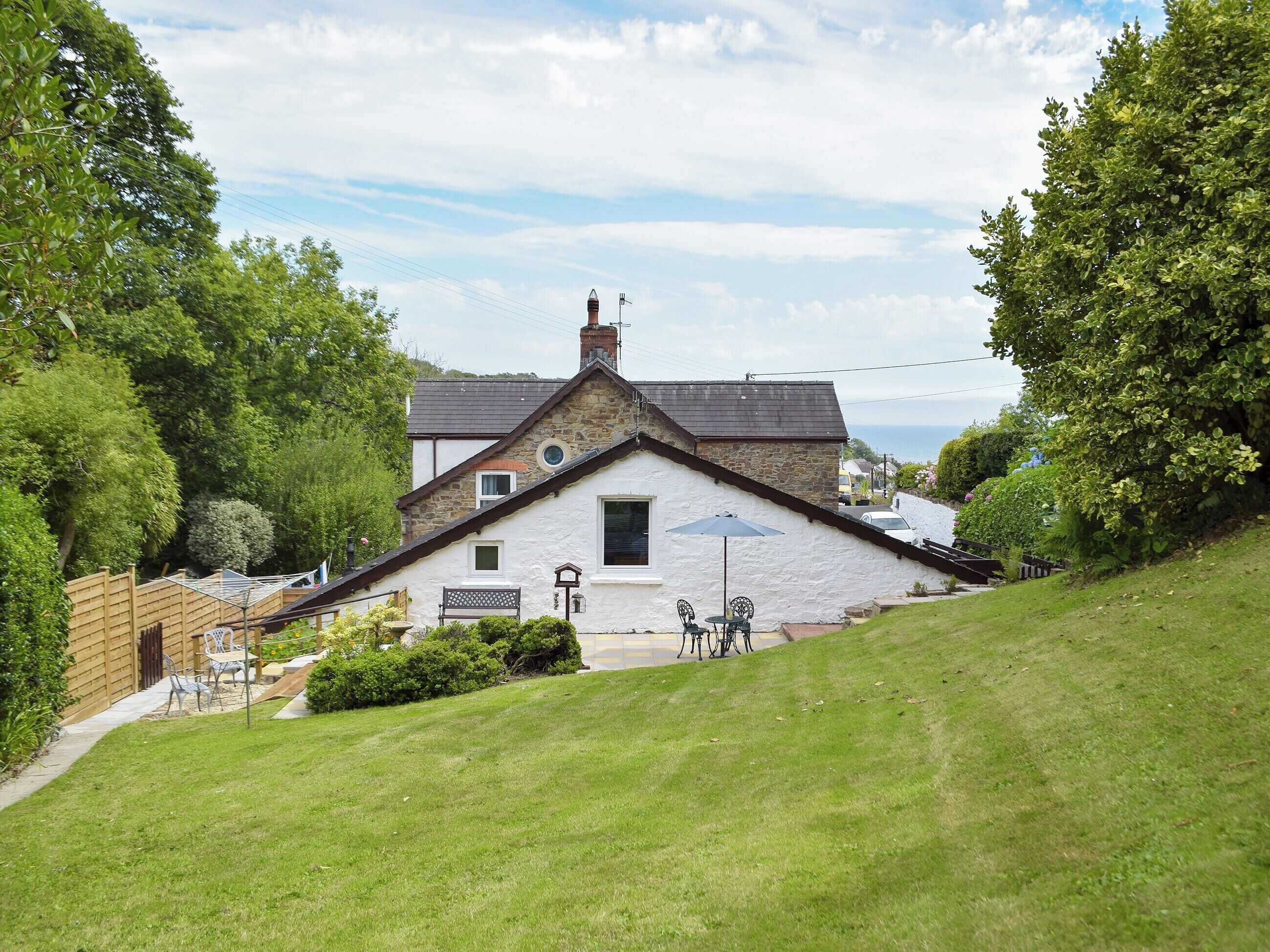 A white house with a stone roof, a small garden, and a view of the sea.