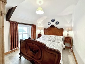 A bedroom with a wooden bed, a window with curtains, a lamp on a bedside table, and a wall with decorative plates. - 4 bedroom accommodation in Combe Martin (Combe Martin)