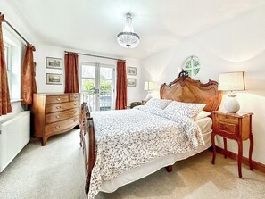 A bedroom with a large bed, a dresser, a nightstand, a lamp, and a chandelier. - 4 bedroom accommodation in Combe Martin (Combe Martin)