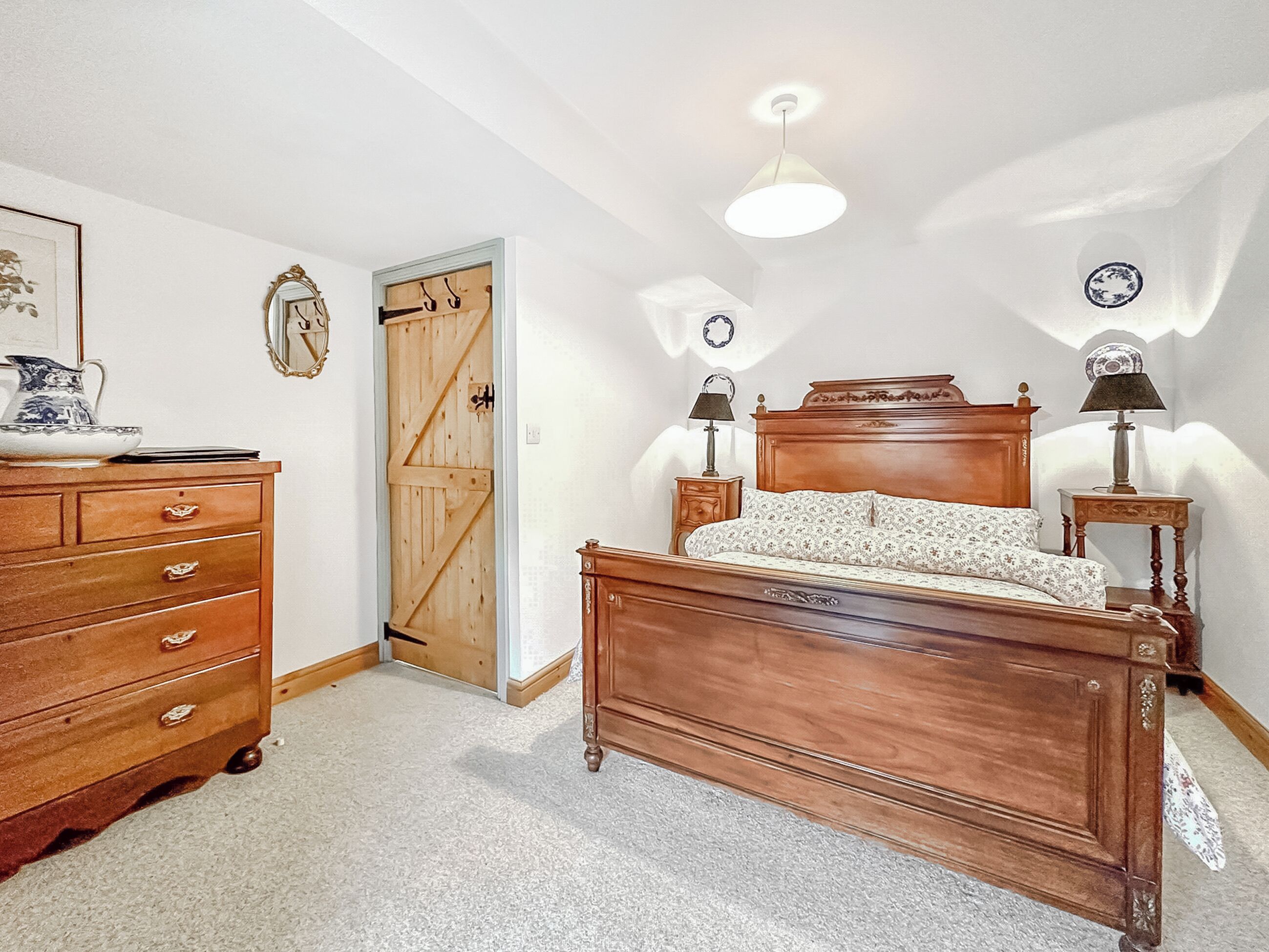 Une chambre à coucher avec un lit en bois, une commode, une porte et un luminaire au plafond.