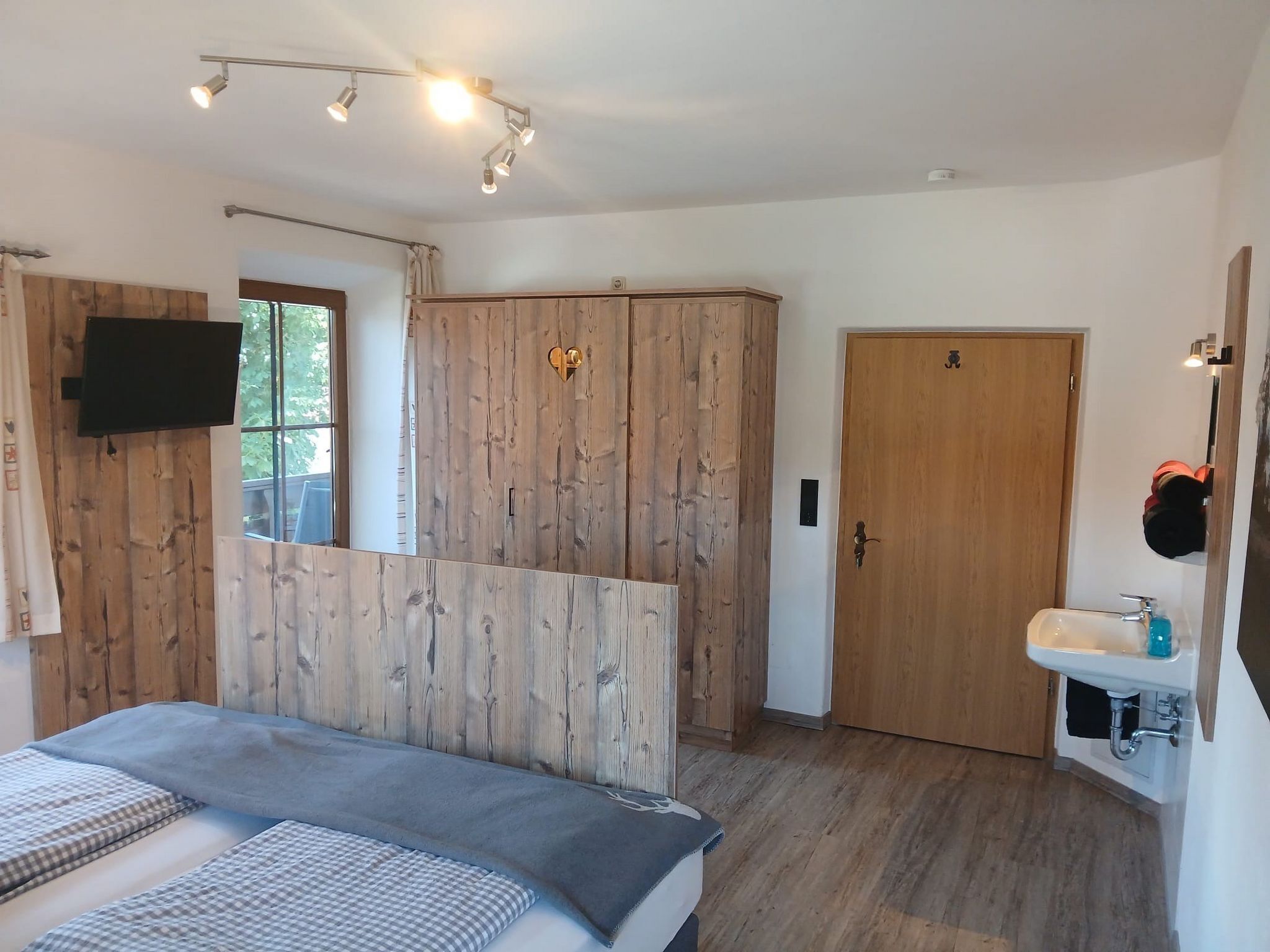 A bedroom with a bed, a wardrobe, a television, a door, and a bathroom with a sink.