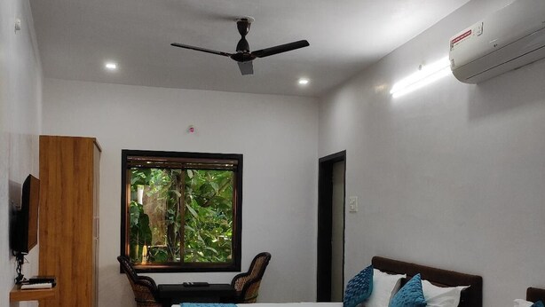 A hotel room with two beds, a ceiling fan, an air conditioner, a window with a view of greenery, and a wooden cabinet. - Hinglaj Palace Hotel Jawai (Bijapur)