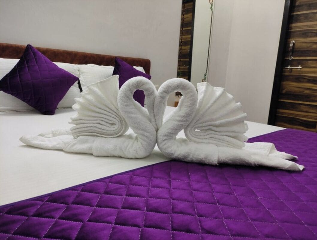 Un lit recouvert d’une courtepointe violette matelassée et agrémenté de deux serviettes blanches disposées en forme de cygnes.