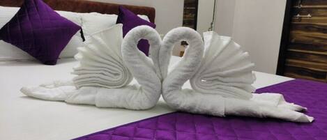A bed with a purple quilted bedspread and two white towels arranged in the shape of swans.