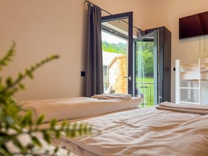 Ein Zimmer mit zwei Betten, einem Fernseher und einem Balkon mit Blick auf Grünflächen.