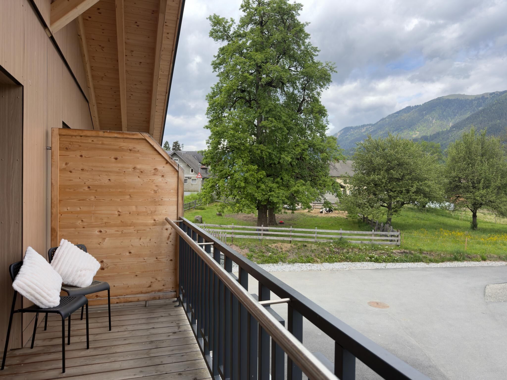 Un balcon en bois offrant une vue sur un arbre et des montagnes.
