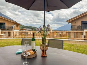A table with a bottle of wine, glasses, a vase with flowers, and a croissant on a terrace with a view of houses and mountains. - Chalet near Nassfeld ski area and Weissensee (Hermagor-Pressegger See)