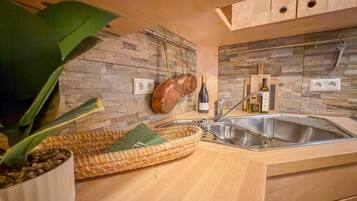 A modern kitchen with a stone backsplash, wooden cabinets, a stainless steel sink, and a potted plant.