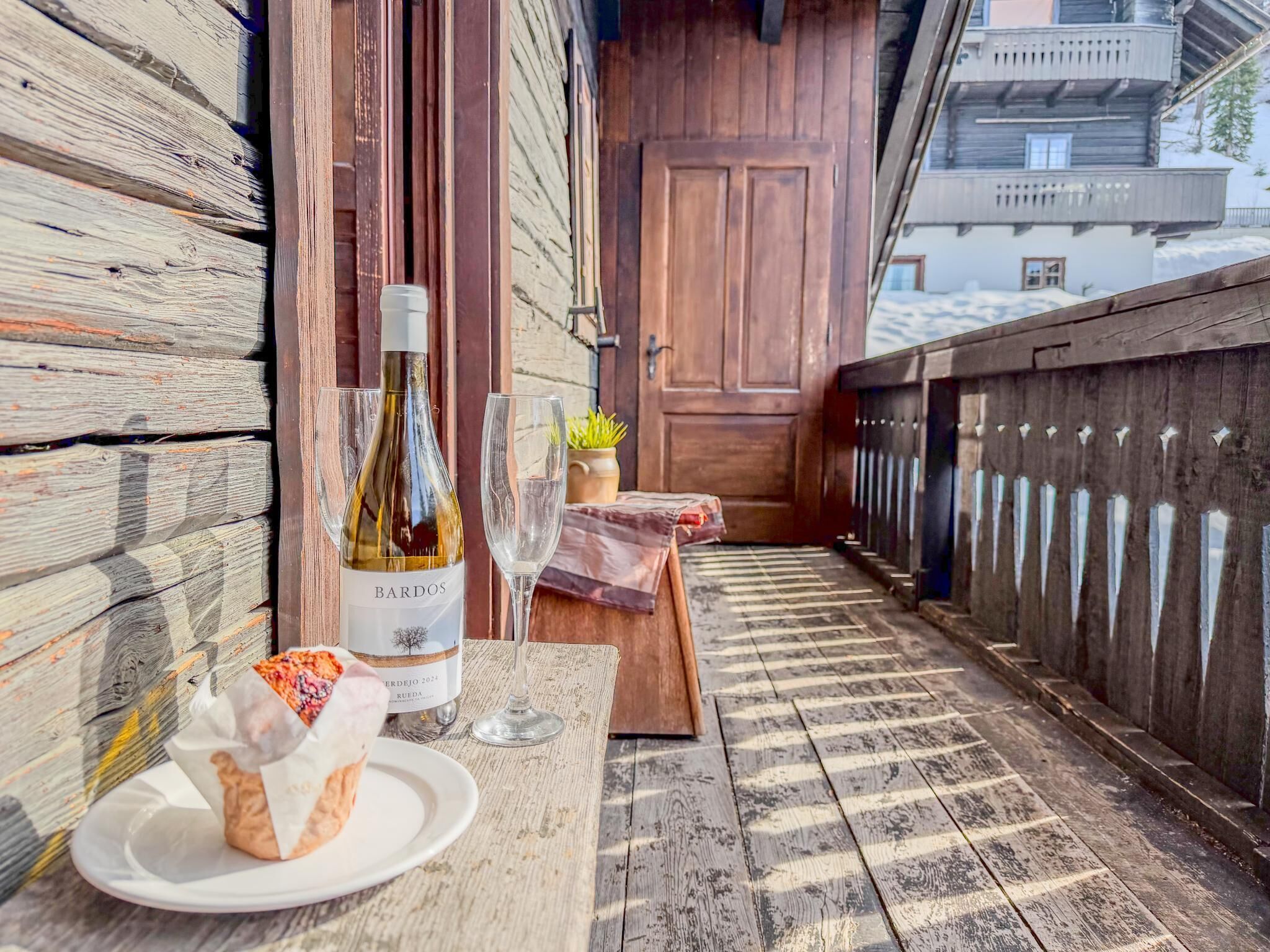 A wooden deck with a table, a bottle of wine, two glasses, and a plate with food.