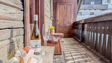 A wooden deck with a table, a bottle of wine, two glasses, and a plate with food.