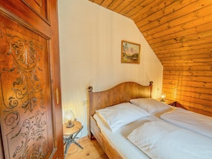 A wooden-paneled room with a bed, a small table with a lamp, and a painting on the wall.