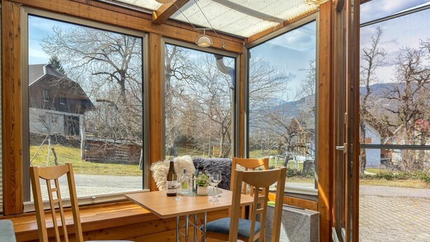 A wooden dining area with a table and chairs, large windows with a view of a rural landscape. - Just a few minutes to the Millennium Express (Tröpolach)