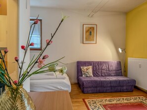 Une pièce avec un canapé violet, une table en bois, un vase rempli de fleurs et un tableau accroché au mur.
