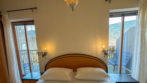 A double bed with two pillows, a wooden headboard, bedside tables with lamps, and large windows with curtains. - Just a few minutes to the Millennium Express (Tröpolach)