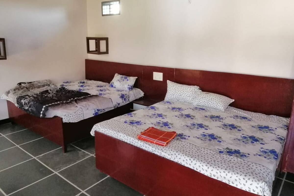 Een kamer met twee bedden, elk met een houten hoofdbord en bloemenbeddengoed. Er is een klein raam in de muur en een stopcontact boven één van de bedden.