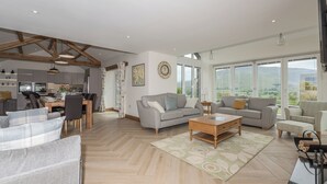Een ruime woonkamer met een eettafel, banken en een groot raam met uitzicht op de omgeving.