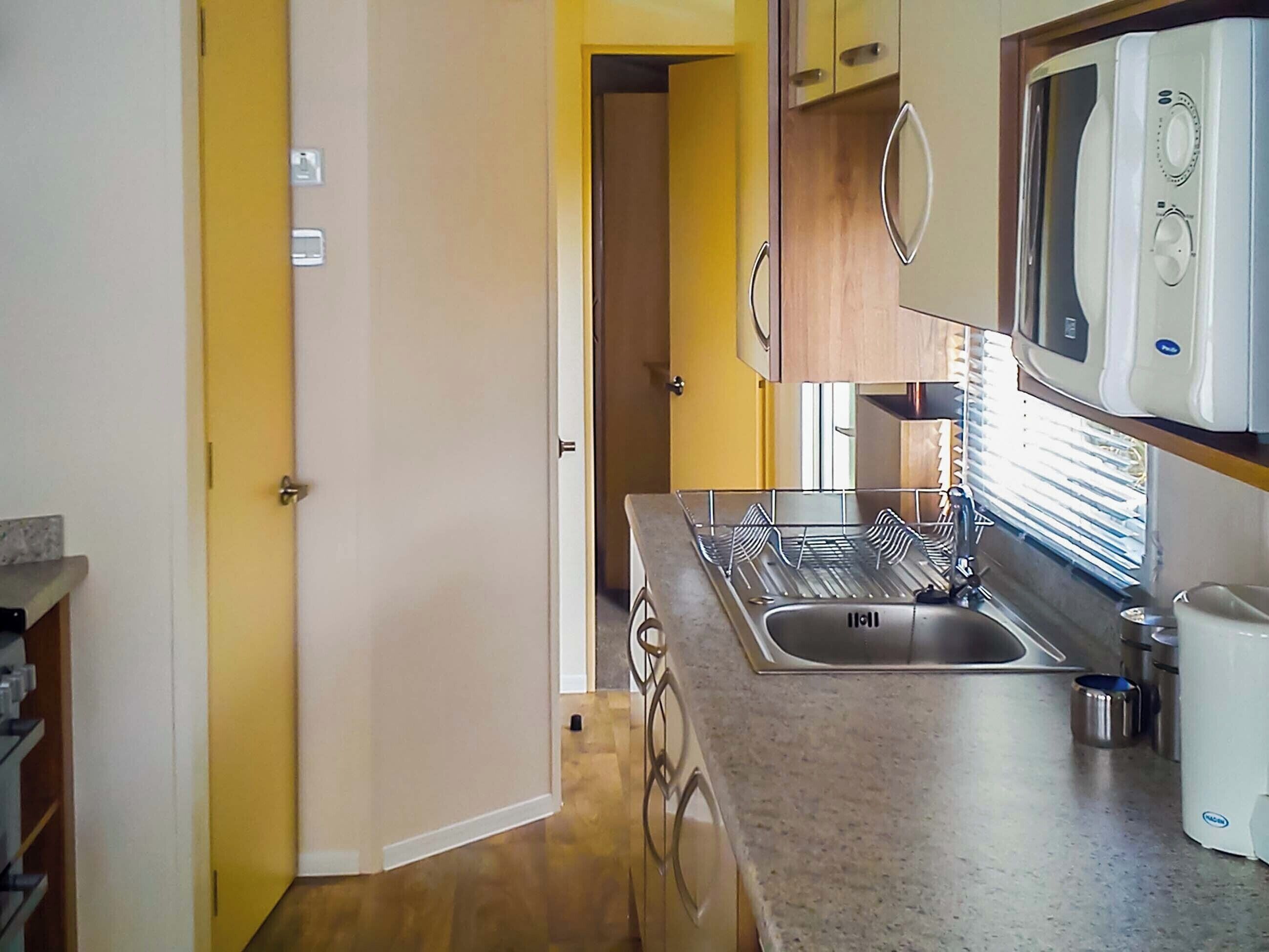 A kitchen with a stainless steel sink, a microwave, and a dish rack.