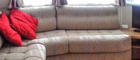 A corner sofa with a red pillow, a wooden side table, and a TV on a stand.