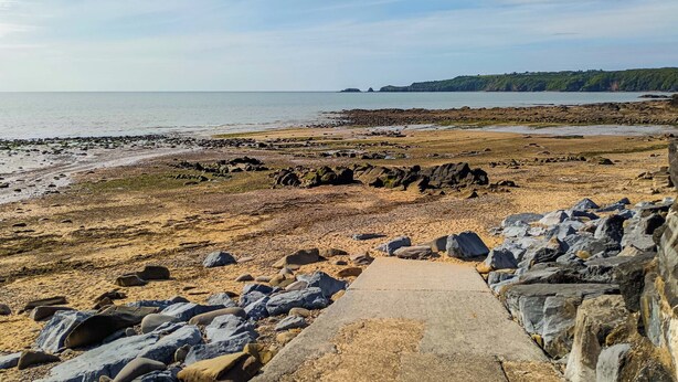 Une plage de galets avec un chemin en béton qui mène à l’eau.