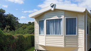 Une maison mobile dotée d’un porche à l’avant, de grandes fenêtres avec des rideaux et d’une clôture verte.