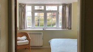 A room with a bed, a wicker chair, a radiator, and a window with curtains. - 2 bedroom accommodation in Staithes, near Whitby (Staithes, near Whitby)