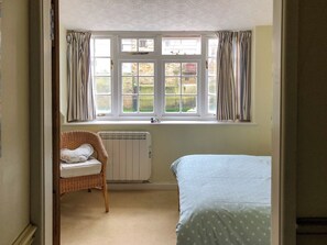 Ein Zimmer mit einem Bett, einem Korbsessel, einer Heizung und einem Fenster mit Vorhängen.