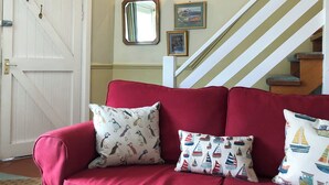 A red sofa with patterned pillows, a white door, and a staircase with a painting above it. - 2 bedroom accommodation in Staithes, near Whitby (Staithes, near Whitby)