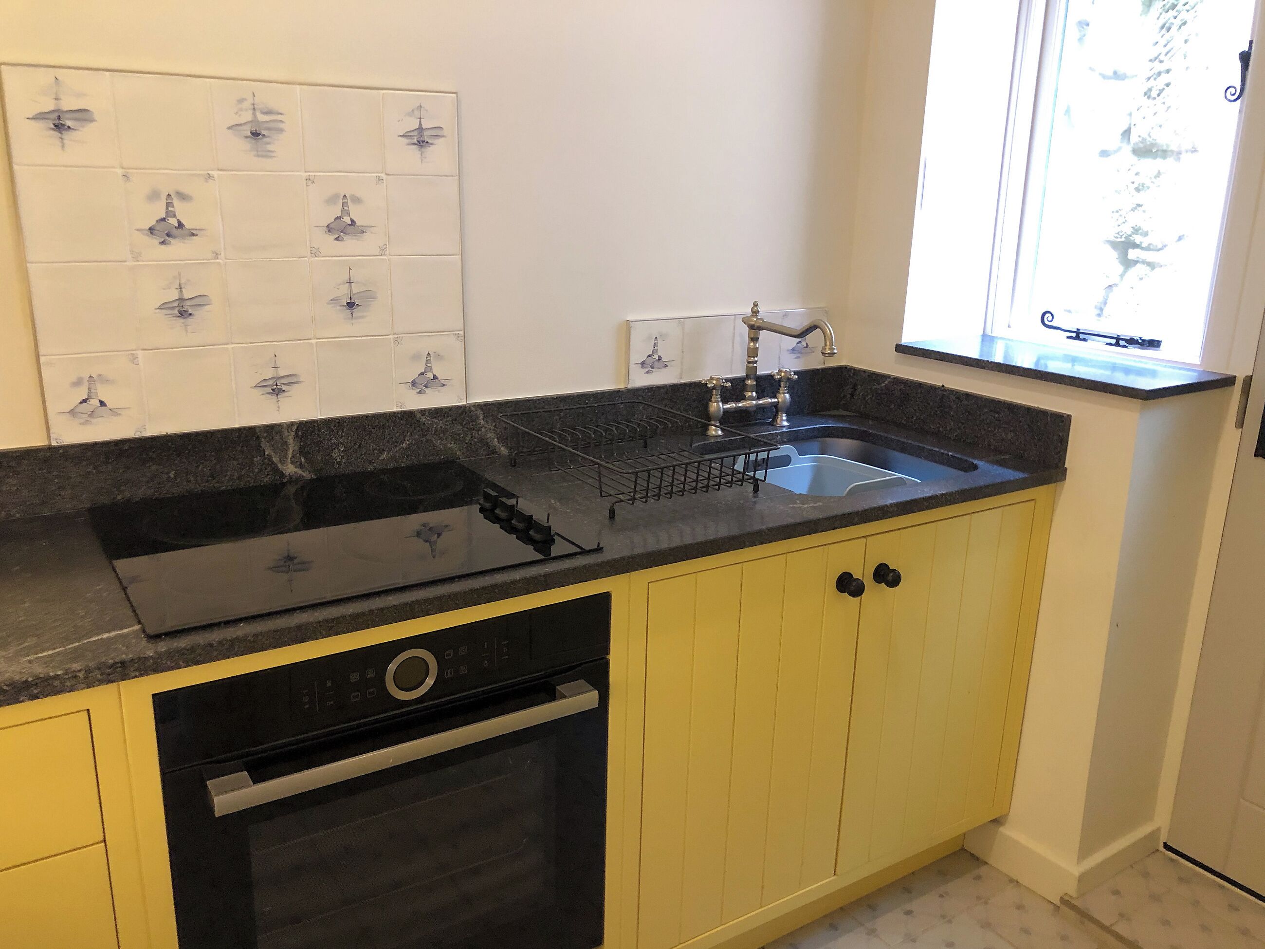 A kitchen with a black stovetop, a sink, and yellow cabinets.
