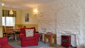 A living room with a red sofa, a wooden dining table, and a stone wall. - 2 bedroom accommodation in Staithes, near Whitby (Staithes, near Whitby)