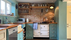 A kitchen with a wooden countertop, a stove, and a sink. There are cabinets and a clock on the wall. - Coastguard's Cottage (Burnham Overy Staithe, near Burnham Market)