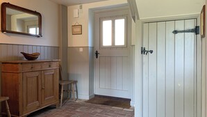 A hallway with a wooden cabinet, a chair, a door, and a window. - Coastguard's Cottage (Burnham Overy Staithe, near Burnham Market)