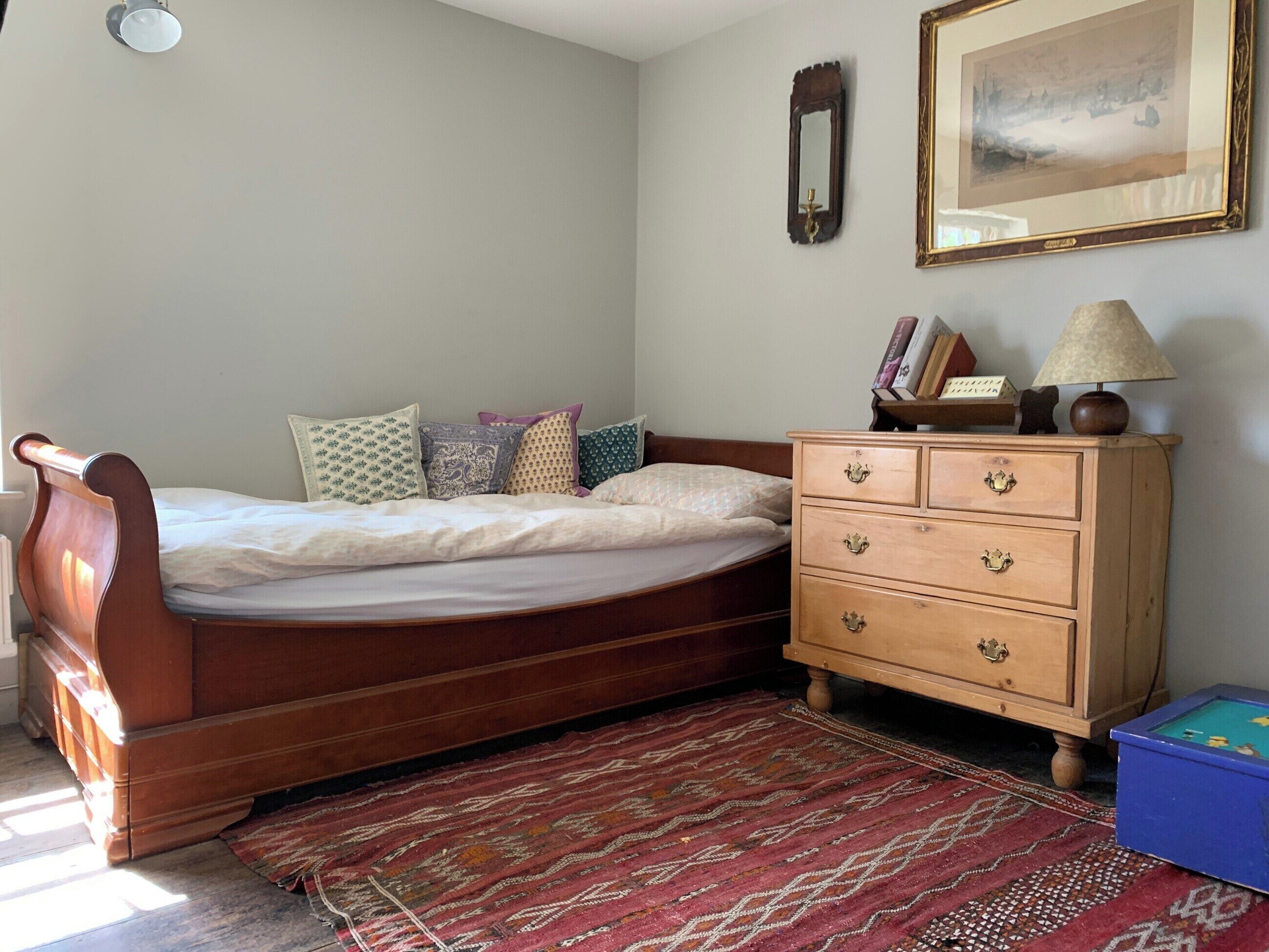 Une chambre à coucher avec un lit en bois, une commode, un miroir et un tableau encadré au mur.